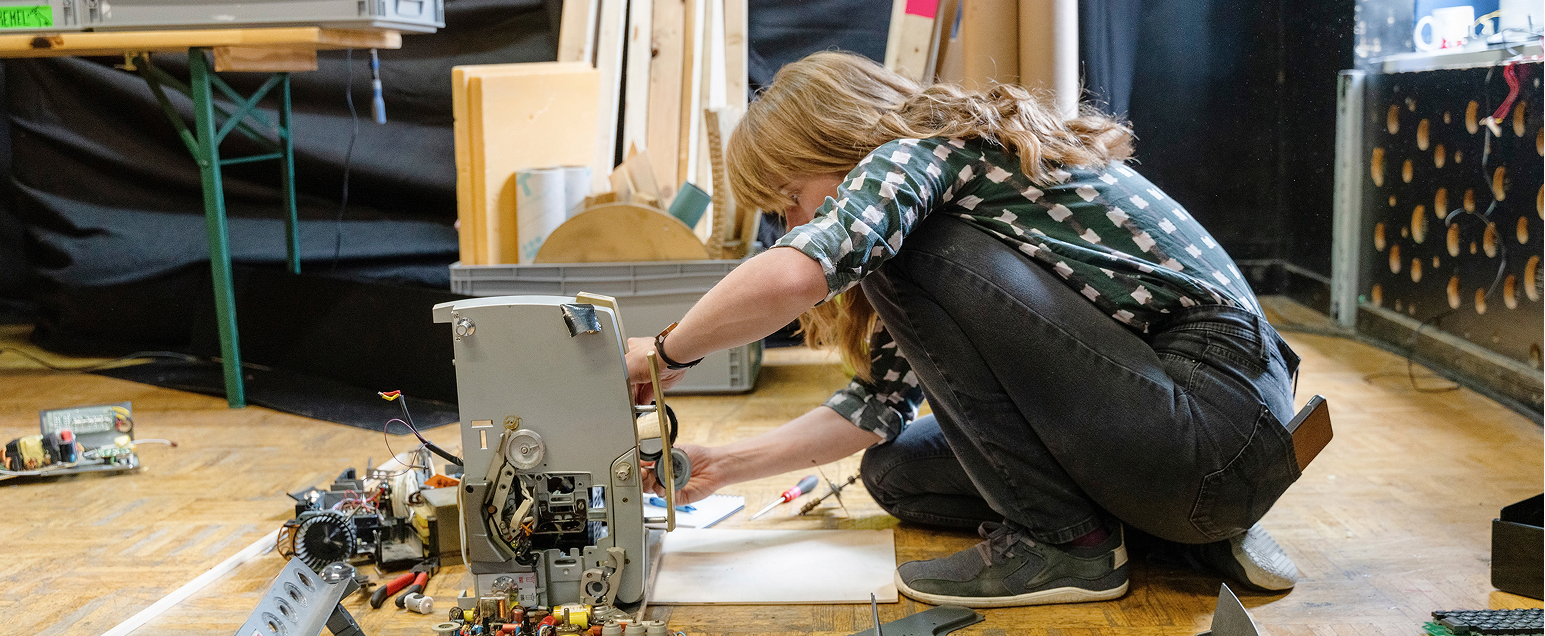 Person schraubt an Objekt am Boden sitzend
