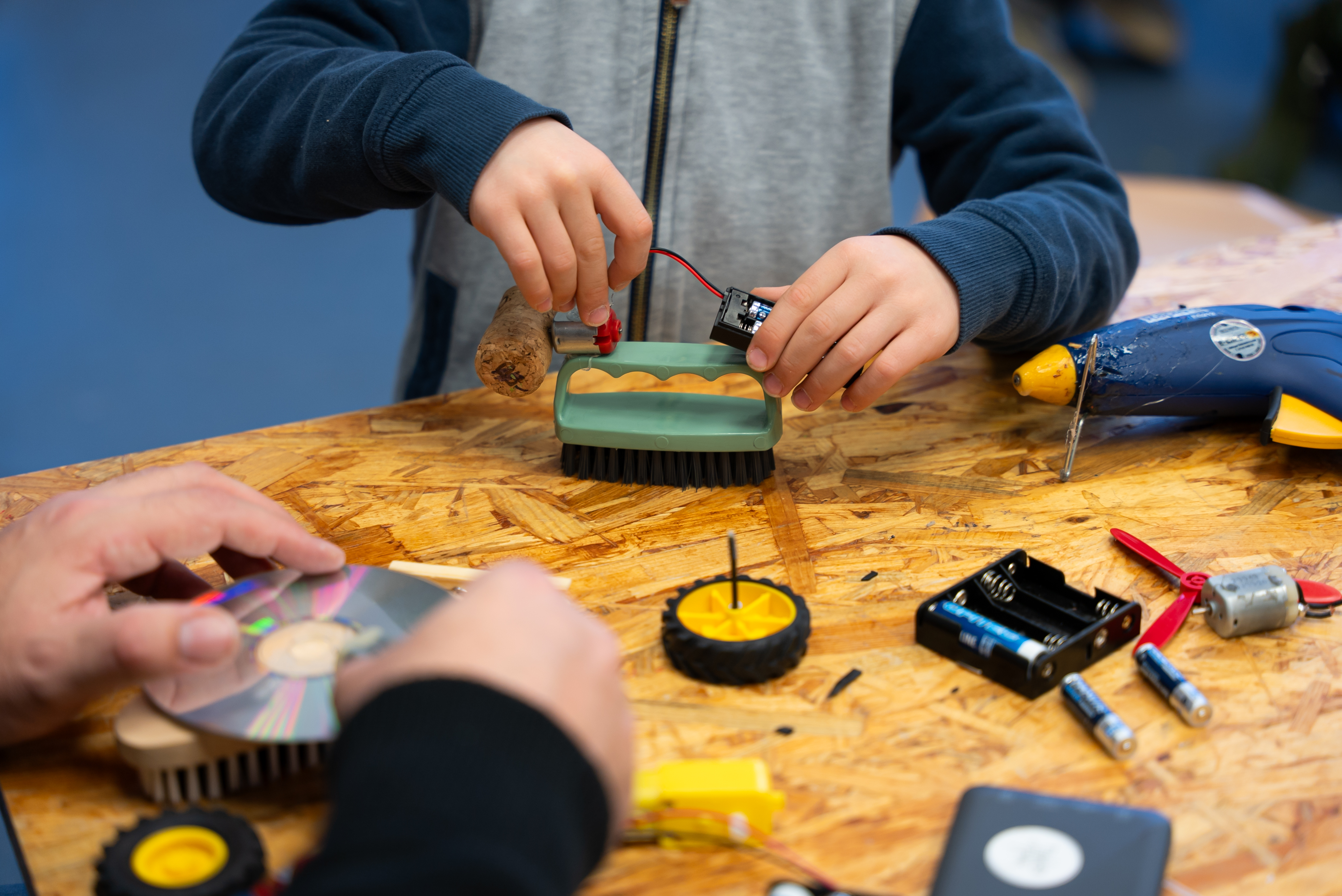 ein kind bastelt aus einer bürste, korken, motoren und weiteren utensilien einen malroboter.